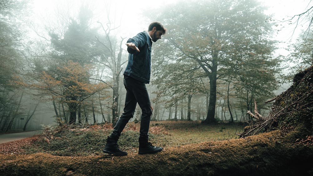 Man in the woods walking, balancing on tree trunk